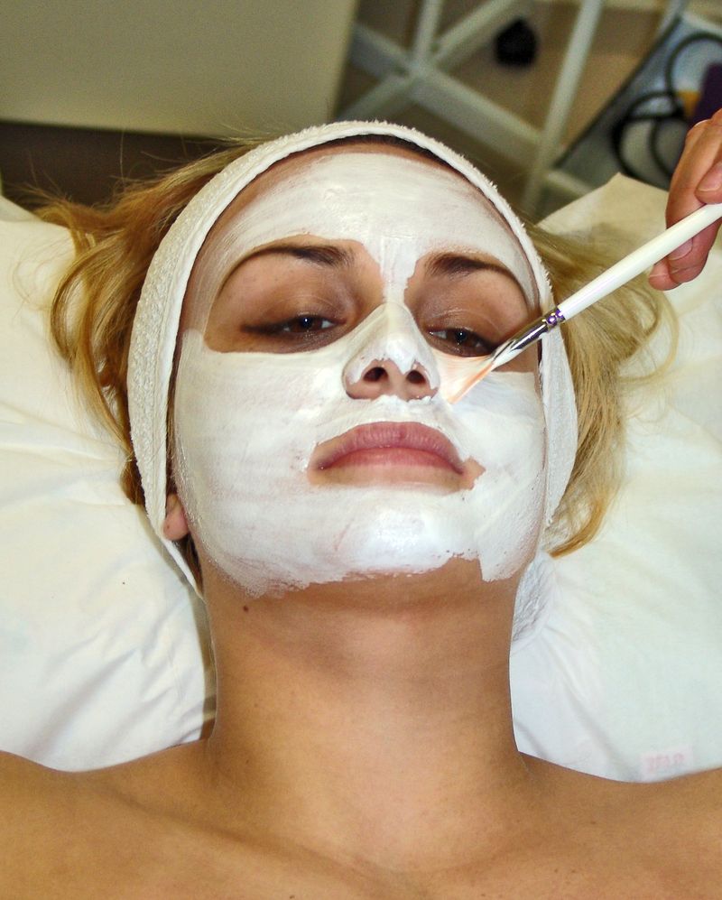 A client lying back in a white headband while a white face mask is brushed on