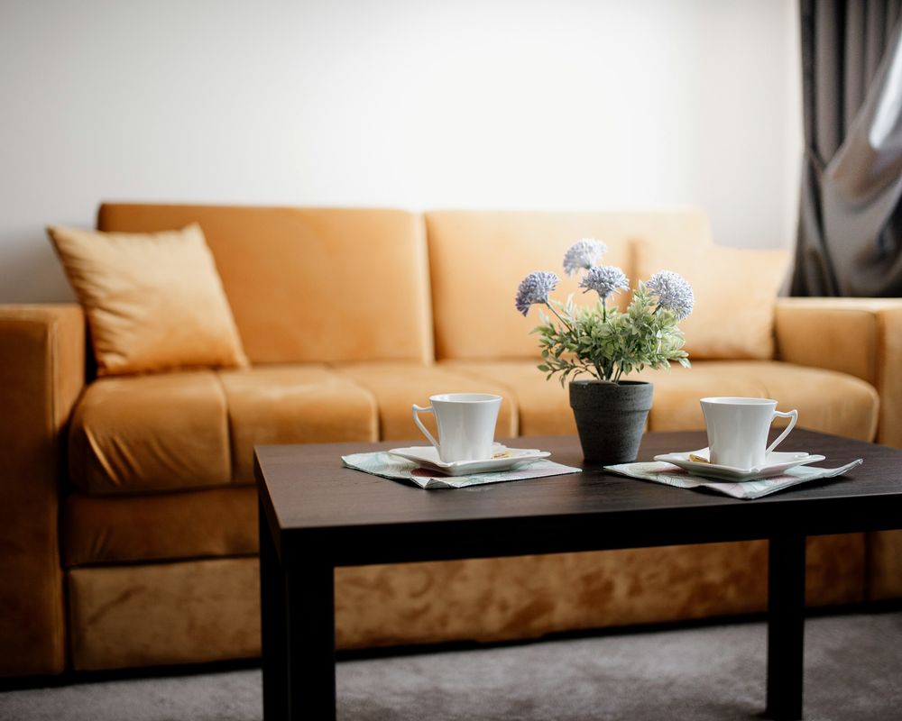 A living room with a tan sofa, cushions and a coffee table set with cups and a small vase of flowers