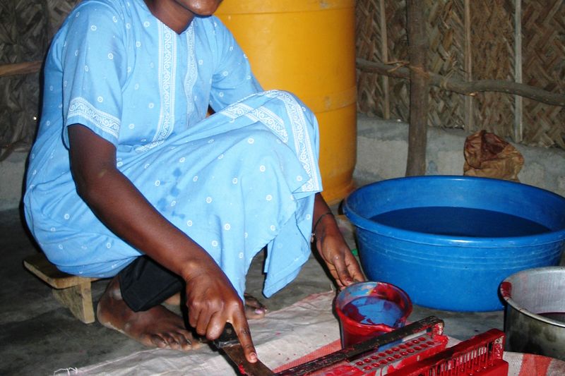 A candle maker at work, cutting coloured wax beside a basin