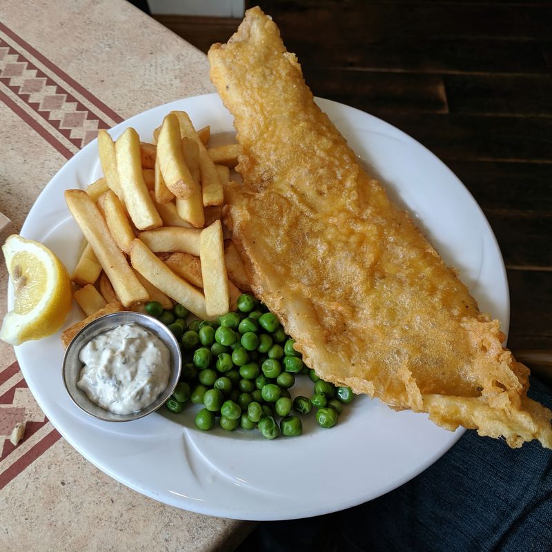 Battered fish and chips with peas, lemon and tartare sauce on a white plate
