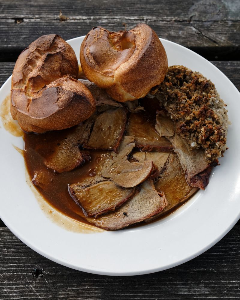 Sliced roast lamb in gravy with Yorkshire puddings and stuffing on a white plate