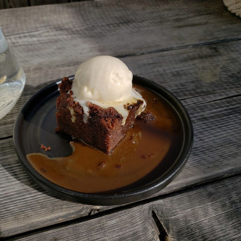 Sticky toffee pudding with ice cream and toffee sauce on a dark plate