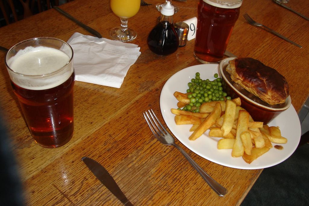 A pint of bitter beside a plate of pie, chips and peas on a pub table