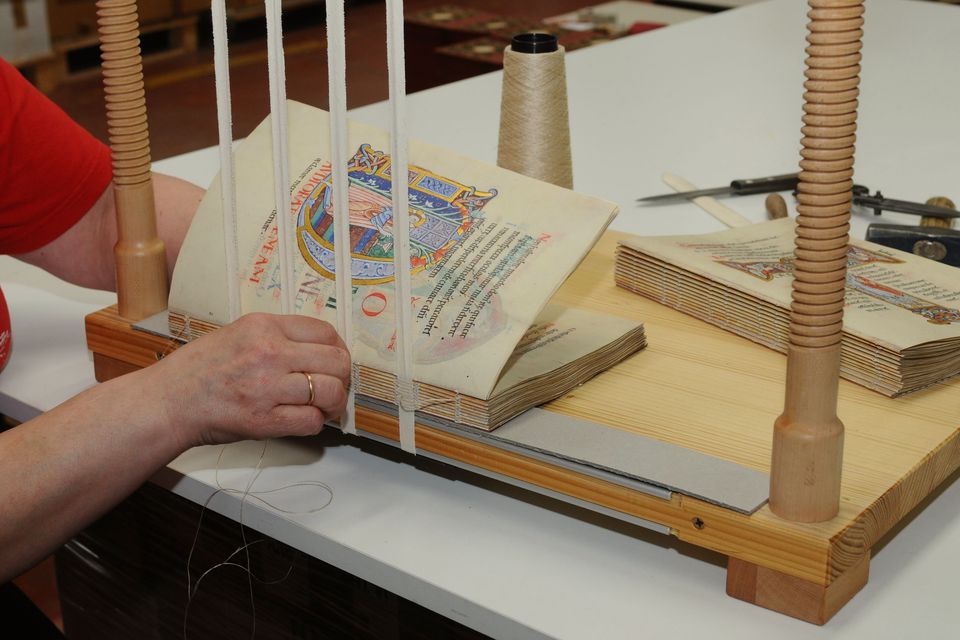 Hands stitching the pages of a book on a sewing frame