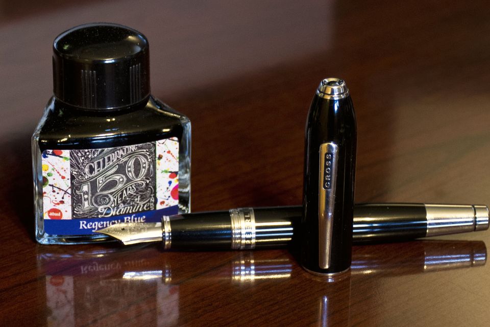 A bottle of ink beside two fountain pens