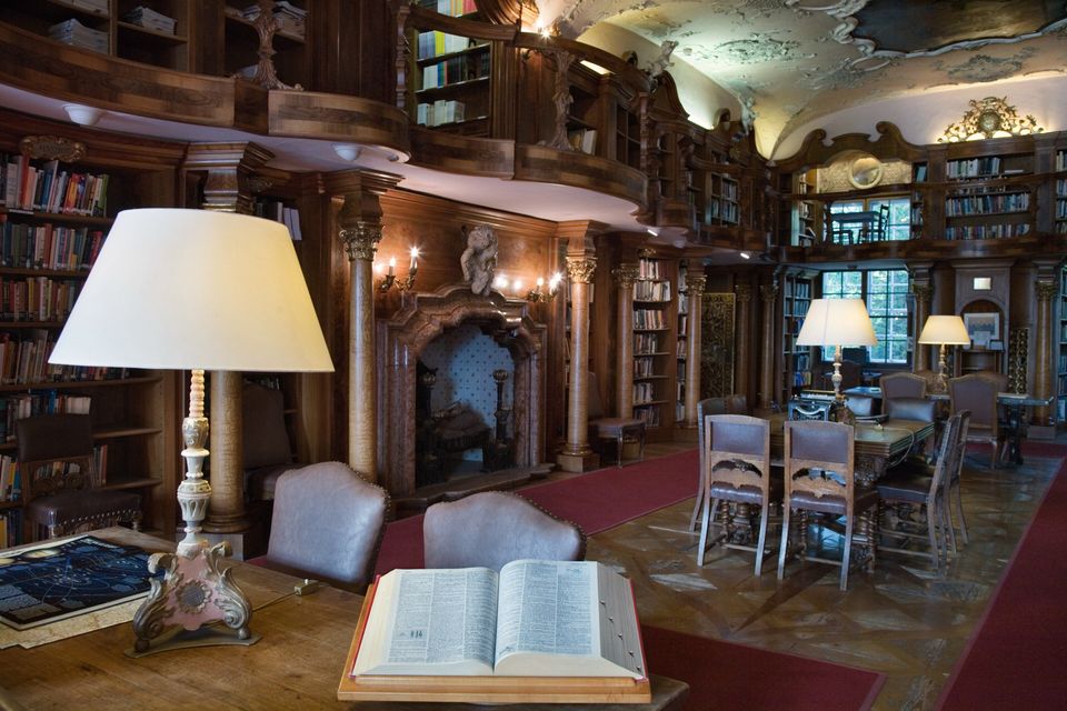 A reading lamp and an open book on a table in a wood-panelled library