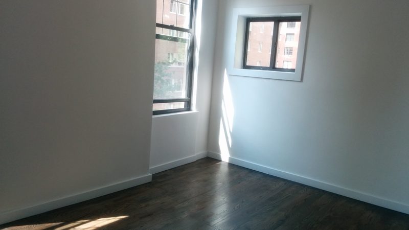 Empty room with dark wooden floorboards, white walls and daylight from two corner windows