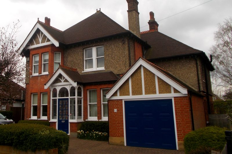 Large detached red-brick house with tile-hung gables, a tall chimney and a blue garage door