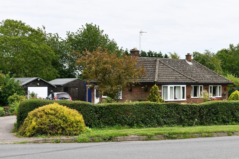 Detached bungalow with a tiled roof behind a clipped hedge and front lawn