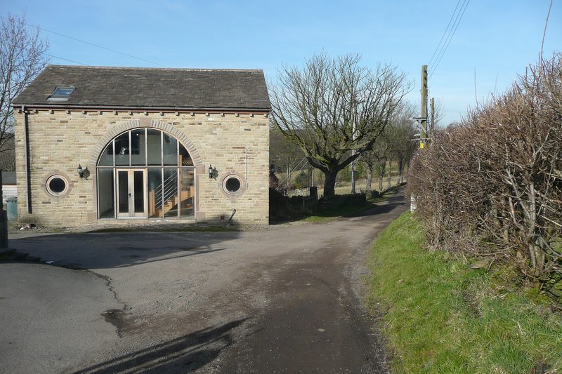 Stone barn conversion with a tall arched glazed opening and a slate roof