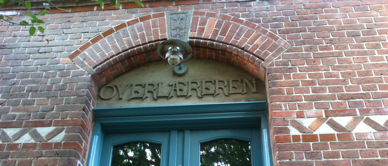 A brick arch with a carved stone keystone above a blue-green double door