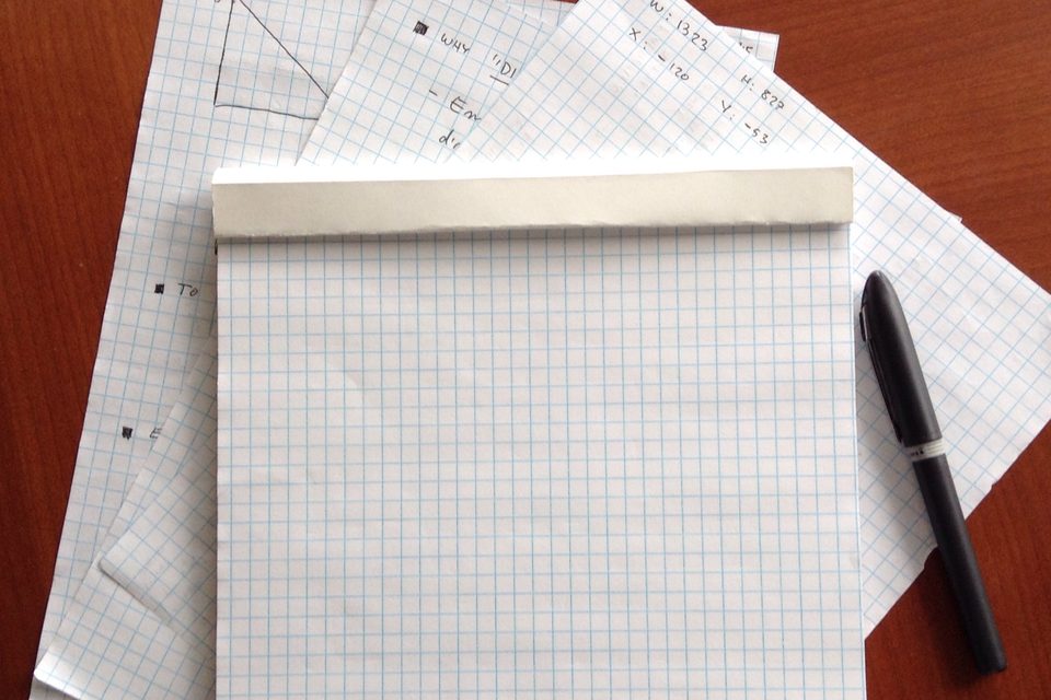 A pad of squared paper and a black pen on a wooden desk