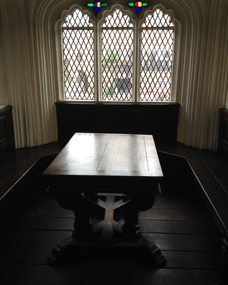 A heavy wooden table beneath a leaded window in a dim library room
