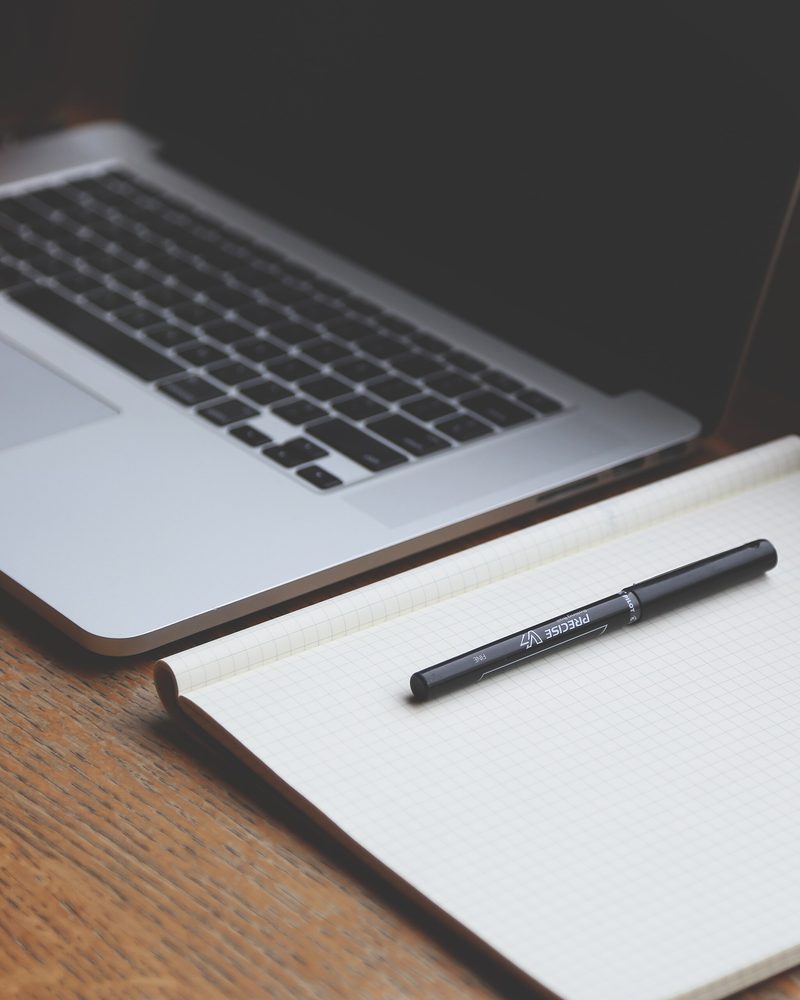 A laptop, a notebook and a pen on a wooden table