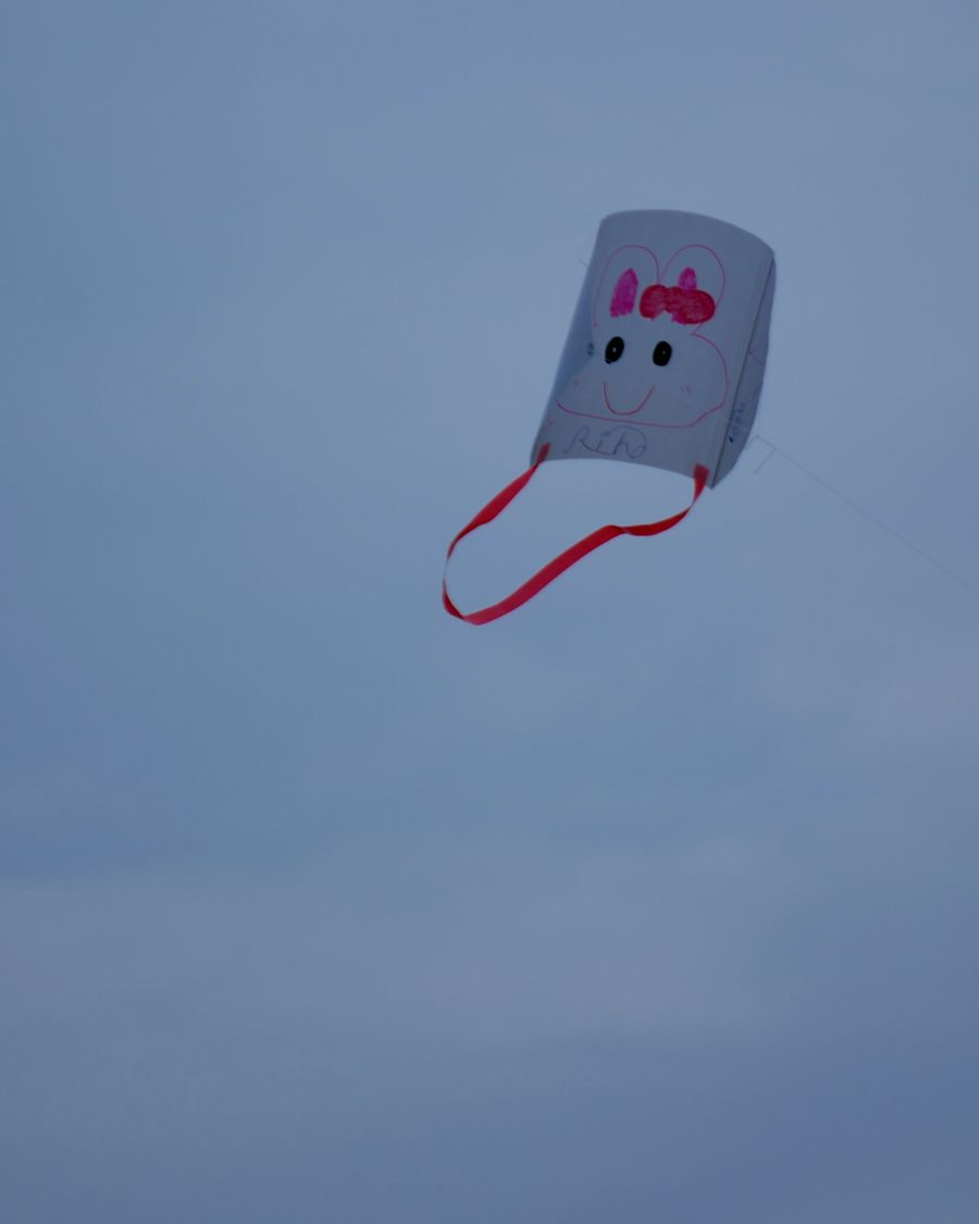 A homemade kite with a hand-drawn smiling face flying against a soft blue-grey sky