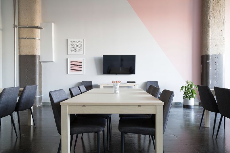 An empty meeting room with a long white table, dark chairs and a screen on the wall