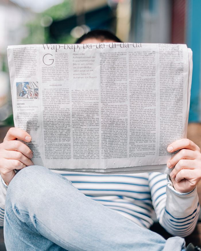 A person on a bench reading a newspaper held up in front of their face