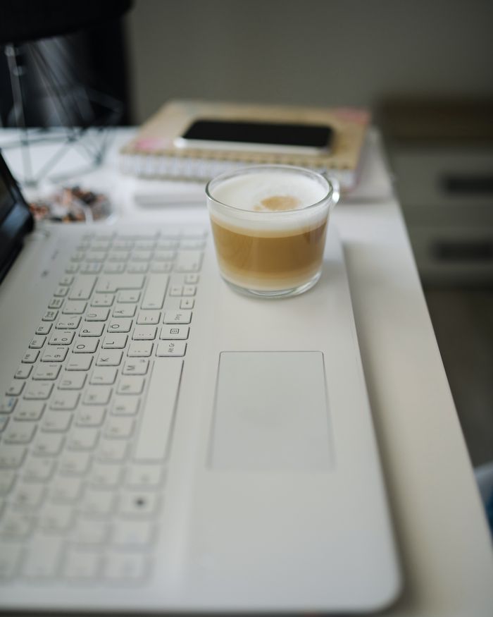 A white laptop on a desk with a glass of iced coffee and a phone just behind it