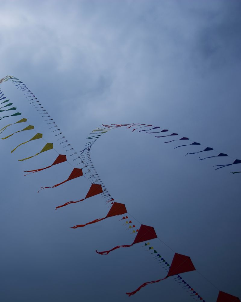 A long string of small kites flying under grey clouds
