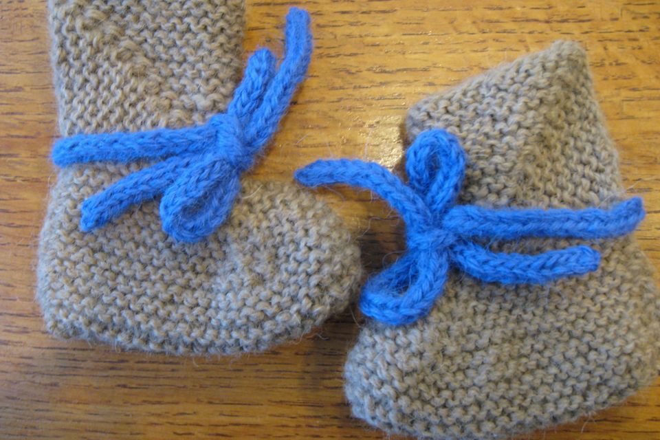A pair of grey hand-knitted baby bootees with blue ties