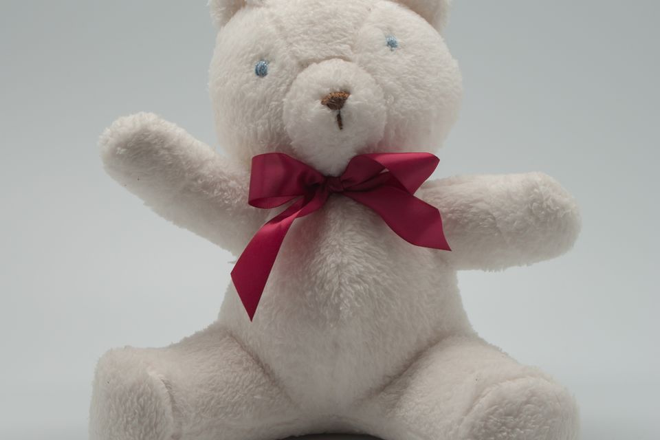 A white handmade teddy bear with a red ribbon bow