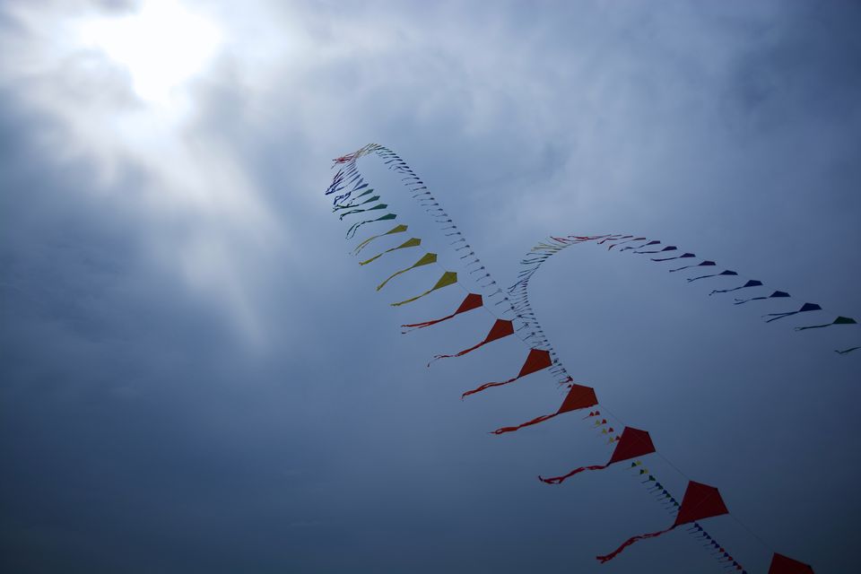A long string of small kites flying under grey clouds