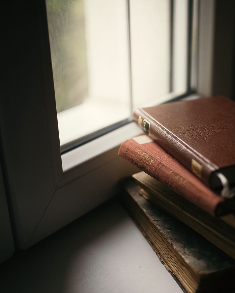 A stack of old books on a windowsill in low light