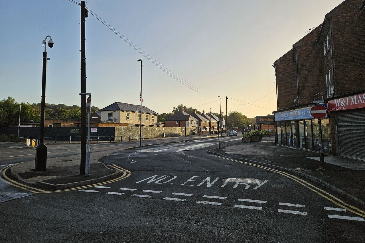 An empty street corner at sunrise, shutters still down on the shops