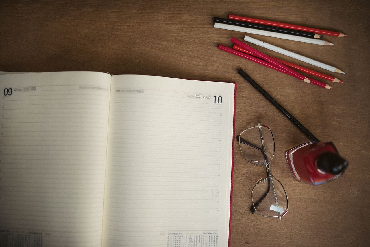 An open notebook, red pencils and a pair of glasses on a wooden table