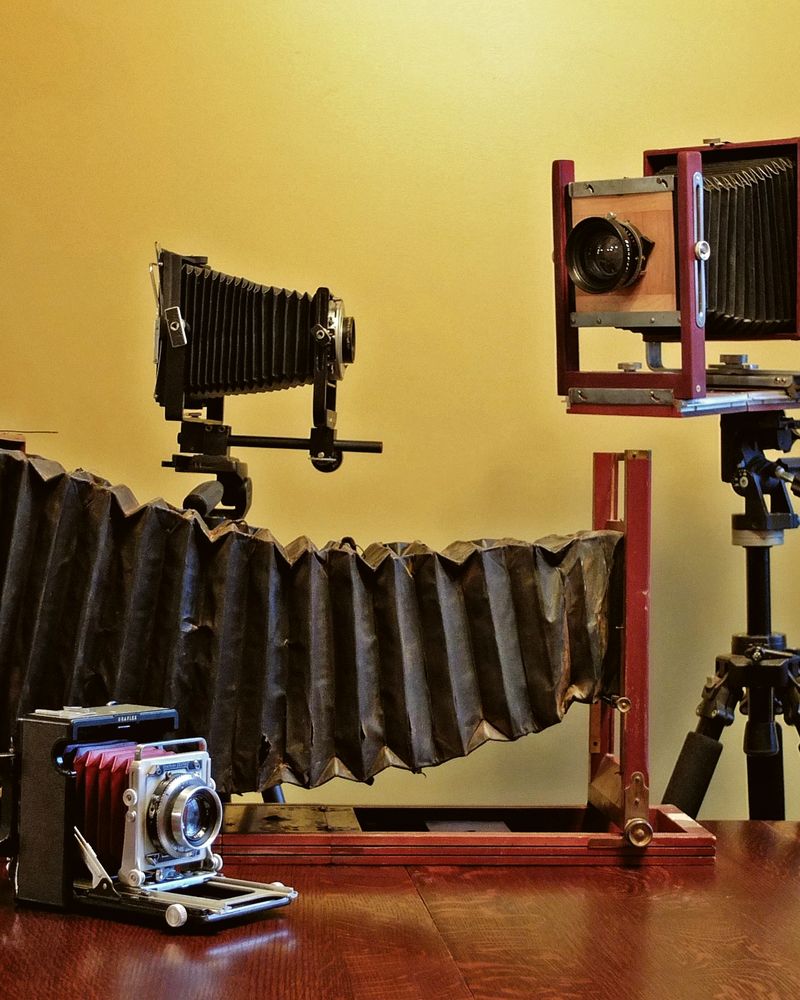 Large-format wooden bellows cameras on tripods against a yellow wall
