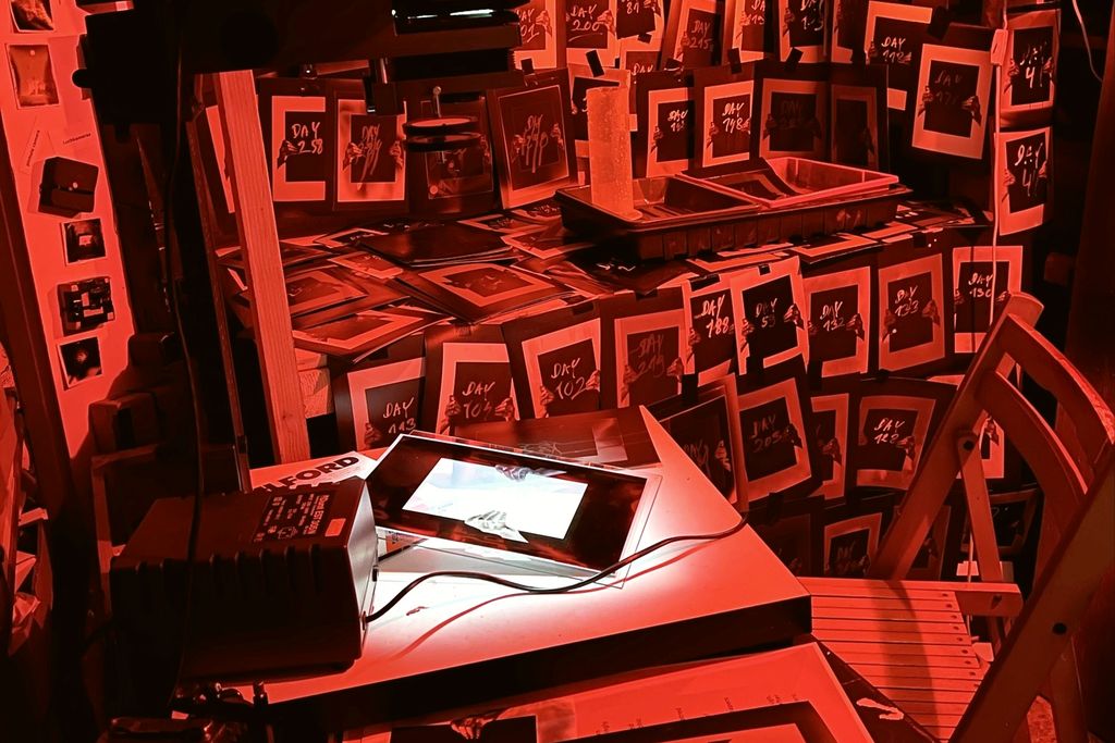 A darkroom lit red, its walls covered in pinned prints