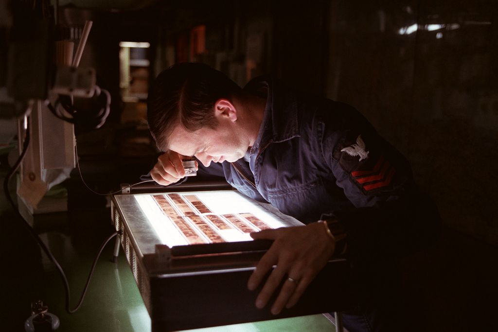A man leaning over a light box, checking film negatives in a dark room