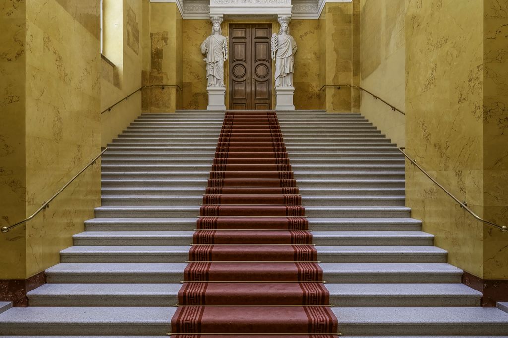 A wide stone staircase with a red runner between yellow marble walls
