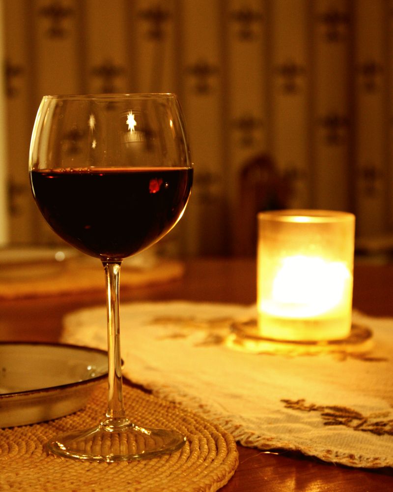 A glass of red wine beside a lit candle on a lace tablecloth