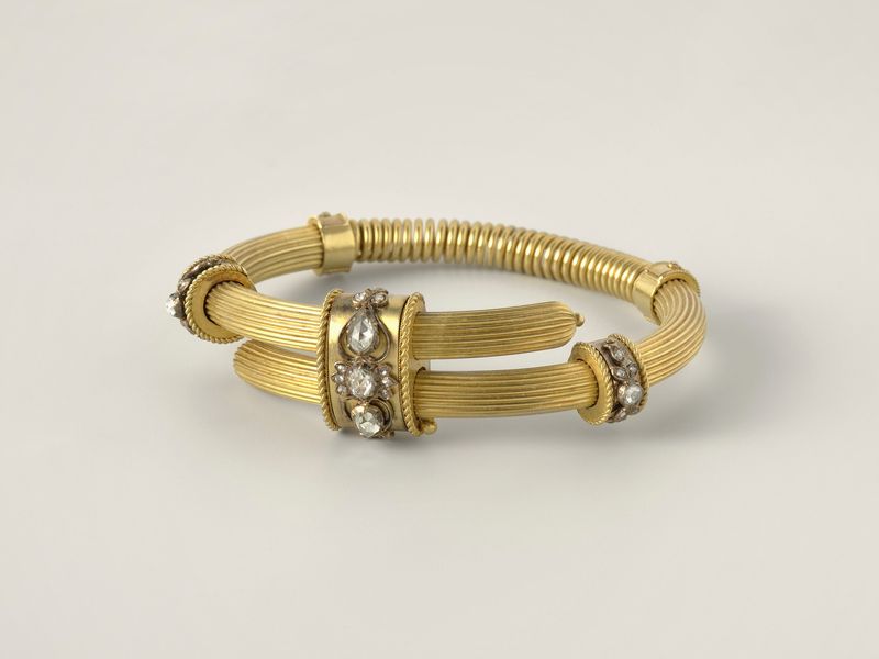 A ribbed gold bangle with a small diamond-set section on each side, on pale grey, library photograph shown for style