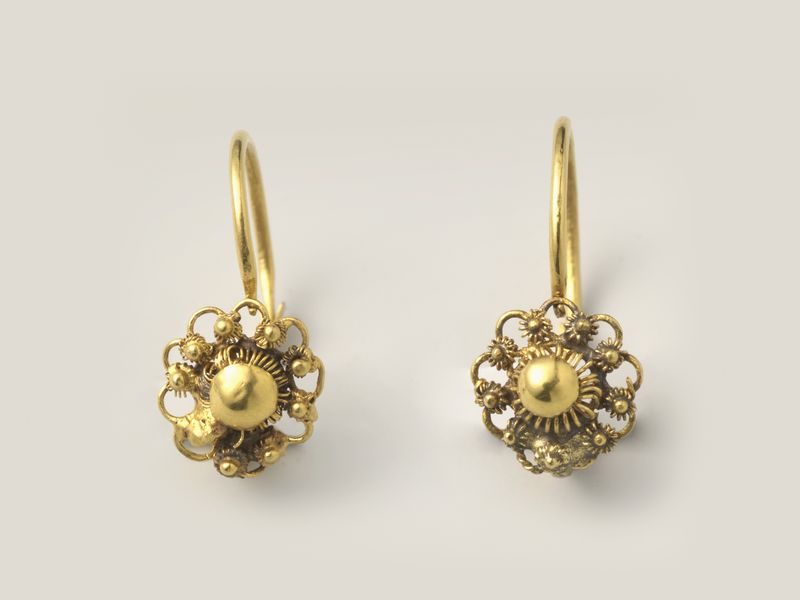 A pair of gold filigree rosette earrings on hooks, on pale grey, library photograph shown for style
