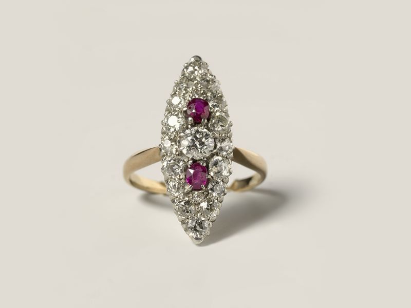 A gold marquise ring set with two rubies at the centre and small diamonds around them, on pale grey, library photograph shown for style