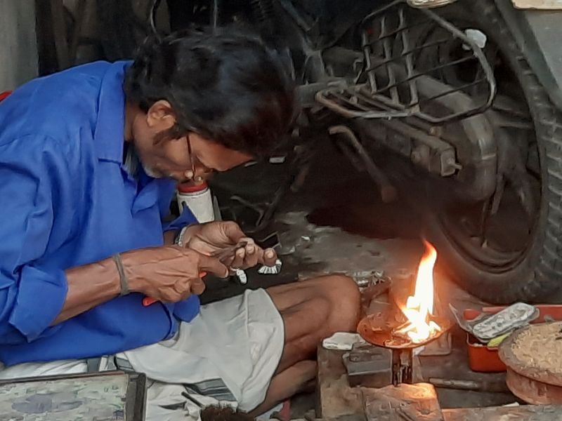 A goldsmith in a blue shirt working on a small piece beside a flame