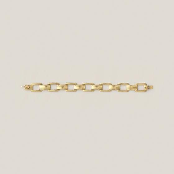 A gold link bracelet with ribbed links, laid straight on pale grey, library photograph shown for style