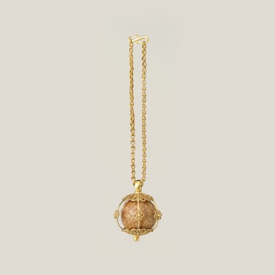 A gold chain with a small round stone pendant in a gold cage mount, on pale grey, library photograph shown for style