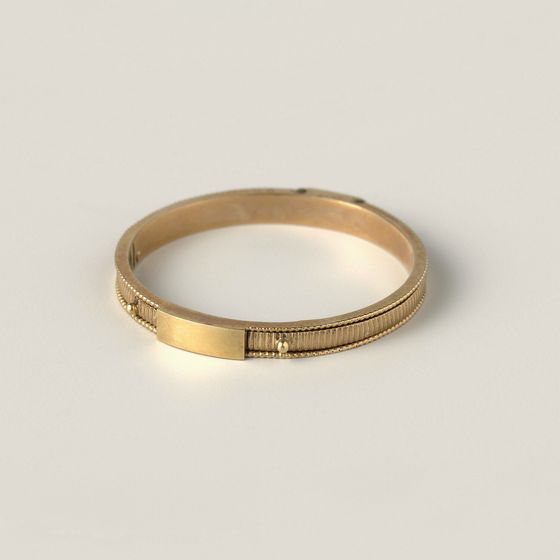 A slim gold band with a small ribbed clasp, on pale grey, library photograph shown for style
