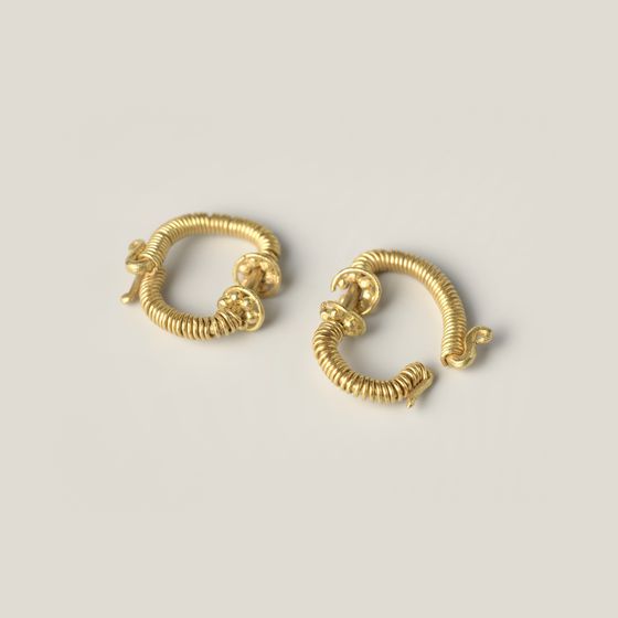 A pair of gold hoop earrings made from wound wire, on pale grey, library photograph shown for style