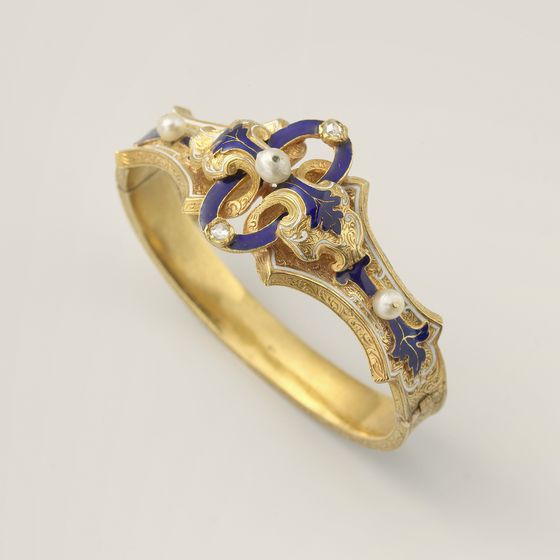 A gold bangle set with diamonds and pearls and blue and white enamel, on pale grey, library photograph shown for style
