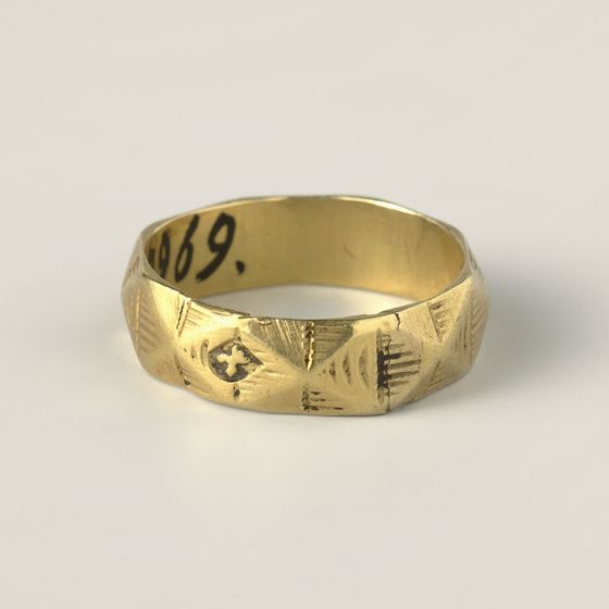 A gold band engraved with lozenges and lettering, on pale grey, library photograph shown for style