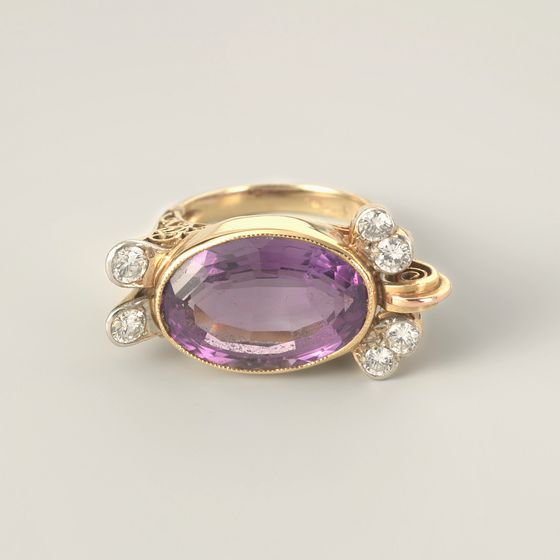 A gold cocktail ring in the form of a turtle, its shell a large oval violet stone set east-west, with small white stones, on pale grey, library photograph shown for style