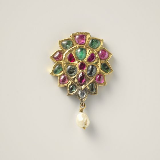 A gold rosette pendant set with red and green stones, with a single pearl drop, on pale grey, library photograph shown for style