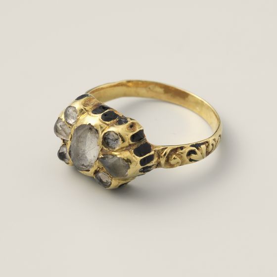 A gold ring with a large central paste stone, small side stones and black enamel, on pale grey, library photograph shown for style