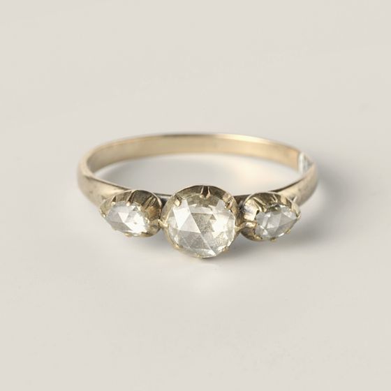 A ring set with three rose-cut diamonds, the largest in the centre, on pale grey, library photograph shown for style