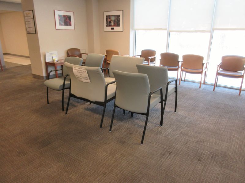 An empty clinic waiting room with spaced-out chairs and tall windows