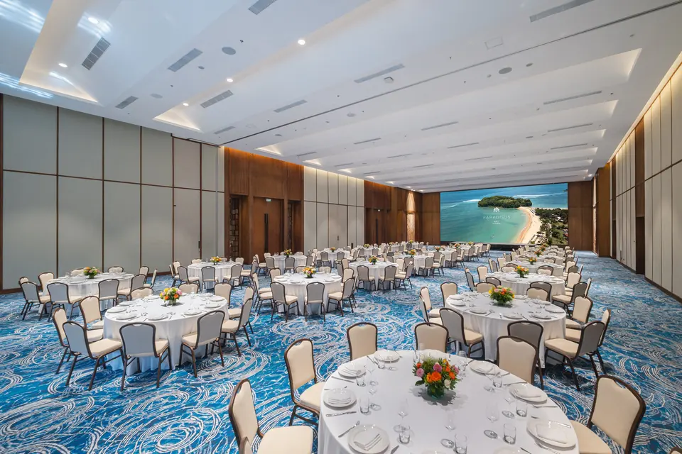 A hotel ballroom with round banquet tables, white chairs and a projection screen